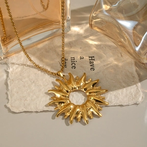 Elegant gold sunburst pendant necklace made of stainless steel on textured paper background