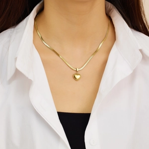 Close-up of polished gold heart pendant necklace on a flat herringbone snake chain