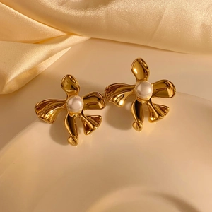Creative gold flower earrings with pearls on white ceramic plate with champagne satin