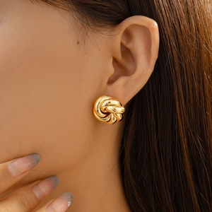 Close-up of model wearing gold twisted swirl earrings with a polished metallic finish