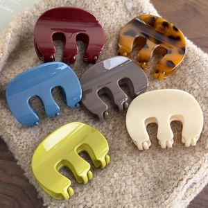 Polished acrylic M-shaped hair claws in six colors displayed on a beige knit background