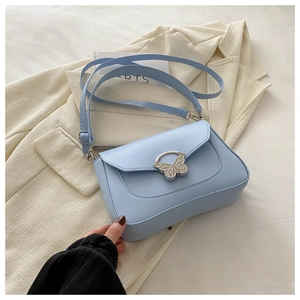 Elegant light blue crossbody bag with a metal butterfly buckle on a beige suit background