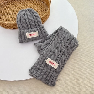 Detail von grauem Zopfstrick-Set aus Mütze und Schal mit roten EIGHT-Buchstaben-Patches