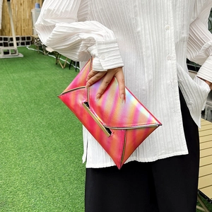 Close-up of pink-orange gradient metallic envelope clutch held against a lawn background