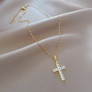 Detailed macro view of a gold-toned cross necklace with cubic zirconia on champagne silk
