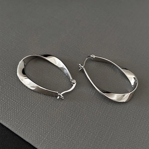 Close-up of silver oval hoop earrings with a twisted metal design on a dark textured base