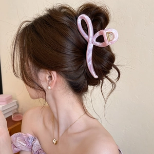 Detail of a pink marble acrylic bow hair claw clip worn on a model's hair in a side view