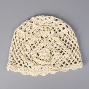 Gros plan du bonnet au crochet crème montrant le motif floral ajouré et le détail perle