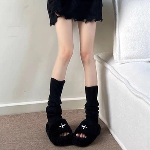 Close-up of black knitted leg warmers styled with fluffy open-toe platform slippers