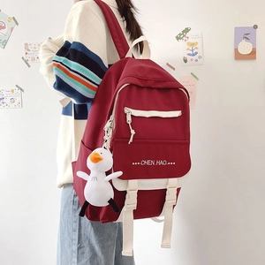 Close-up of red and white canvas backpack with duck charm and side pocket details