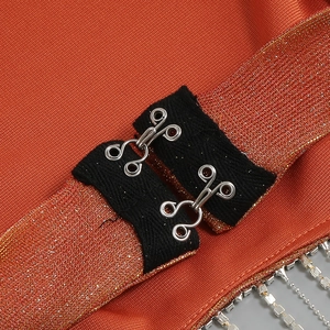 Dettaglio del top in maglia arancione con chiusura a gancio metallico e frange di strass