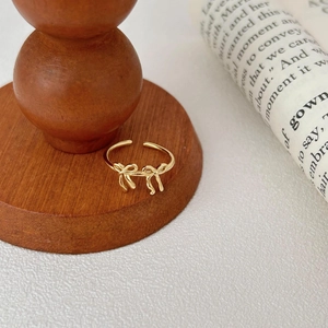 Detail of adjustable gold bow ring on a wooden base with a vintage paper background