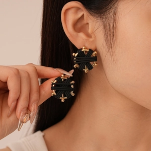 Close-up of gold-tone metal round compass earrings with black woven faux leather detail