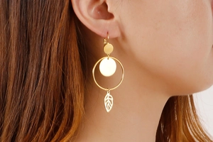 Detailed close-up of golden geometric earrings with solid discs and hollow leaf pendants