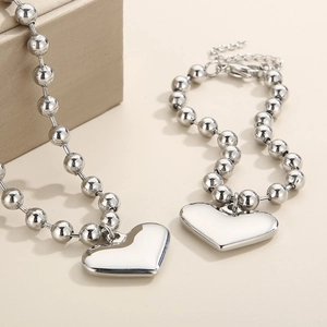 Detailed view of silver beaded necklace and bracelet set with polished heart charms