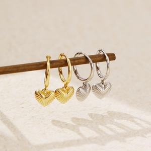 Detail view of gold and silver heart charms on hoops hanging from a wooden stand
