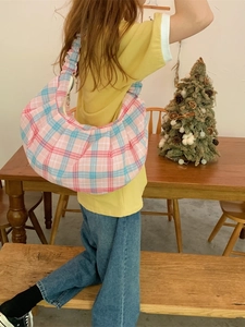 Pink and blue checkered crescent shoulder bag with pleated handle shown in a cozy setting
