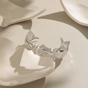 Detail shot of silver fish-shaped open bangle on textured ceramic background