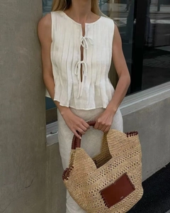 Close-up of woven straw tote bag with brown leather handles and brand logo tag