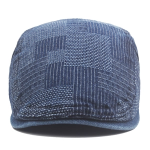 Detailed close-up of blue denim flat cap showing textured patchwork and stripe patterns