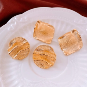 Detail of 18k gold plated round earrings with wavy and grid textures on a white ceramic plate