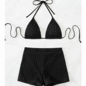 Two-piece black ribbed bikini set with halter top and high-waisted shorts on marble background