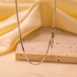 Close-up of silver snake chain necklace with delicate bow pendant on satin background