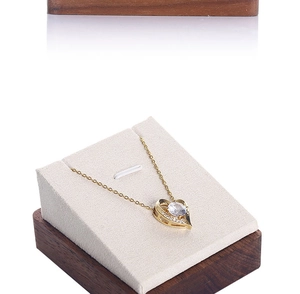 Close-up of heart-shaped gold necklace with large center stone on beige wood stand