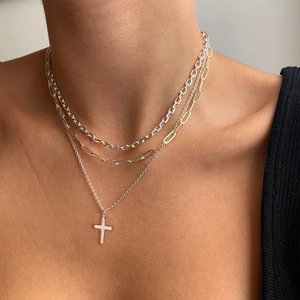 Close-up of layered necklaces including a 18K gold clip chain and a silver cross pendant