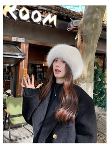 Close-up of fluffy white faux fur bucket hat styled with a black wool coat in outdoor scene