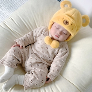 Dettaglio tutina in maglia beige con cappello a orsetto giallo su tessuto bianco