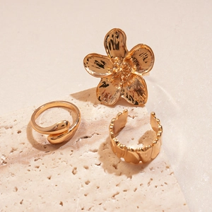 Macro shot of 3-piece gold irregular flower rings on textured beige stone surface