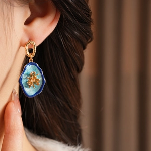 Detail of vintage-style gold flower earring with blue enamel worn by a model