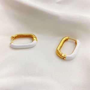 Close-up of gold-plated U-shaped earrings with white enamel finish on silk fabric