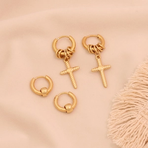 Gold stainless steel hoop earrings with cross and bead charms on pink fabric background
