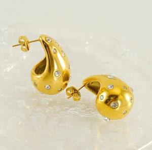 Macro shot of 18K gold water drop earrings with inlaid zircons on a textured glass base