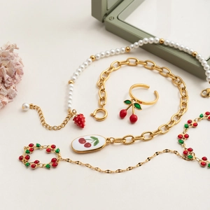Artistic layout of red cherry and strawberry charms on a gold bracelet and pearl necklace