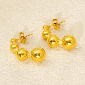 Close-up of golden graduated bead C-shaped hoop earrings on beige textured fabric