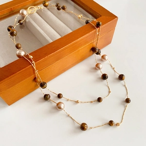 Detail of double-layer gold chain with tiger eye stones and pink pearls on a wooden box
