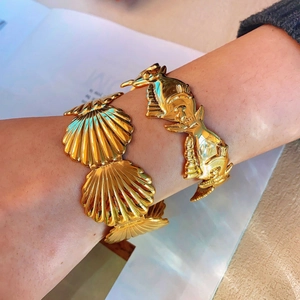 Elegant gold scallop and tropical fish cuff bracelets worn on wrist for a stylish look