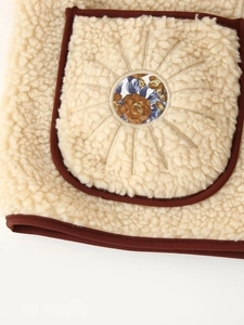 Detailed close-up of beige fleece vest featuring brown piping and floral patch embroidery