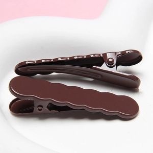 Detail showing two dark brown wavy metal hair clips with a high-gloss finish on a white tray