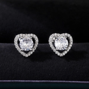 Macro shot of silver heart studs with round center stone on black velvet lining