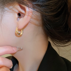 Close-up of 18K gold plated U-shaped twisted earring worn on ear showing glossy metal