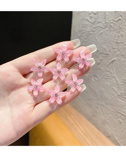 Gros plan de sept mini barrettes fleurs roses avec strass tenues dans une main