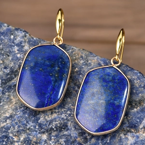 Macro shot of lapis lazuli earrings with golden geometric frames on raw blue stone