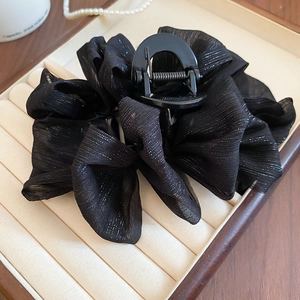 Detail of large black hair claw clip with pleated shimmering fabric on a jewelry tray