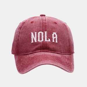 Close-up of NOLA white embroidery on washed red cotton baseball cap with vintage texture