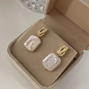 Detailed macro view of baroque rectangle pearl earrings with textured golden metal plating