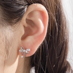 Close-up of a silver bow knot zircon stud earring worn by a model in titanium steel